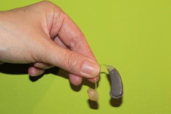 Stock photo of hand holding hearing aid on green background